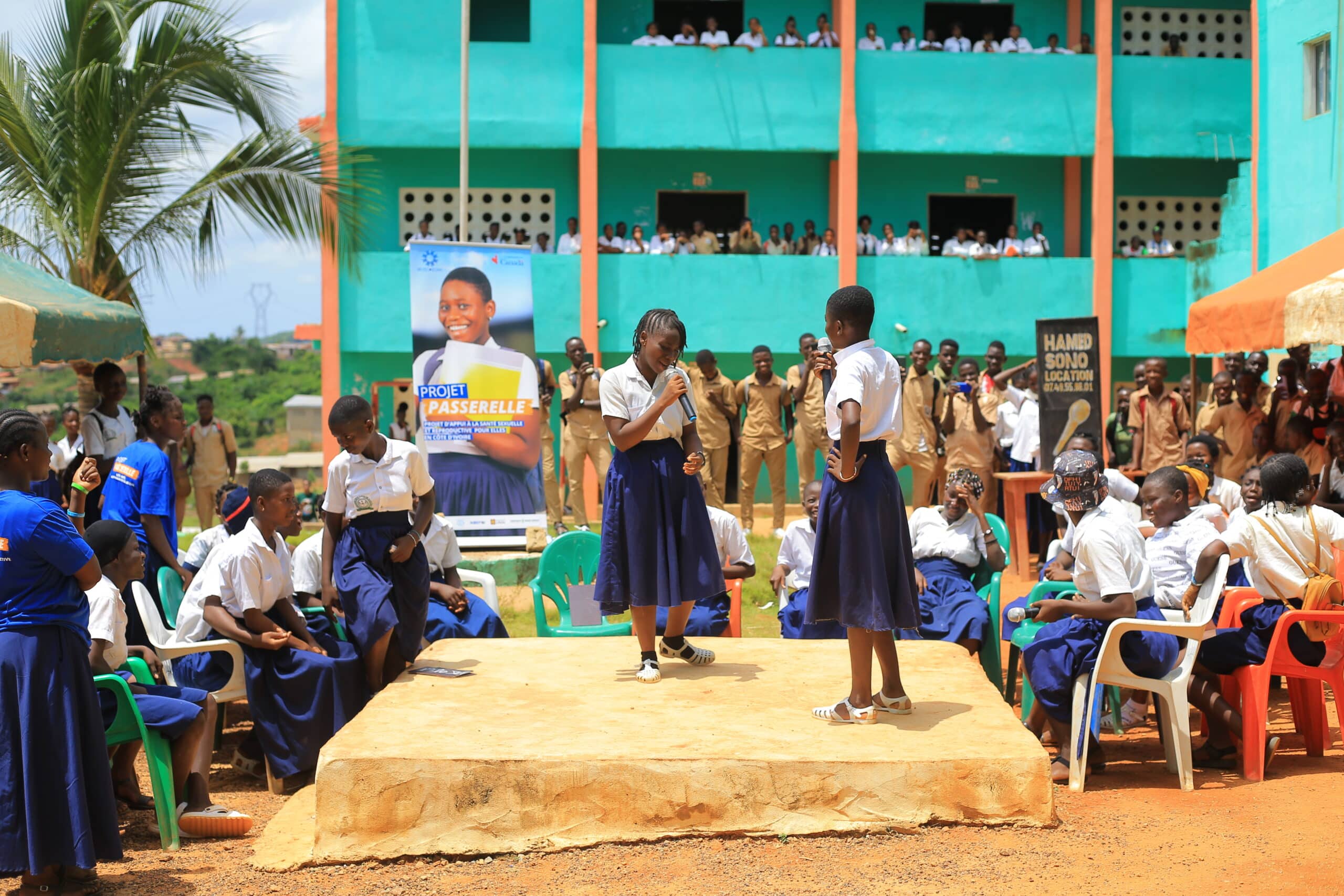 Two girls perform a play about the importance of education on a stage surrounded by their classmates