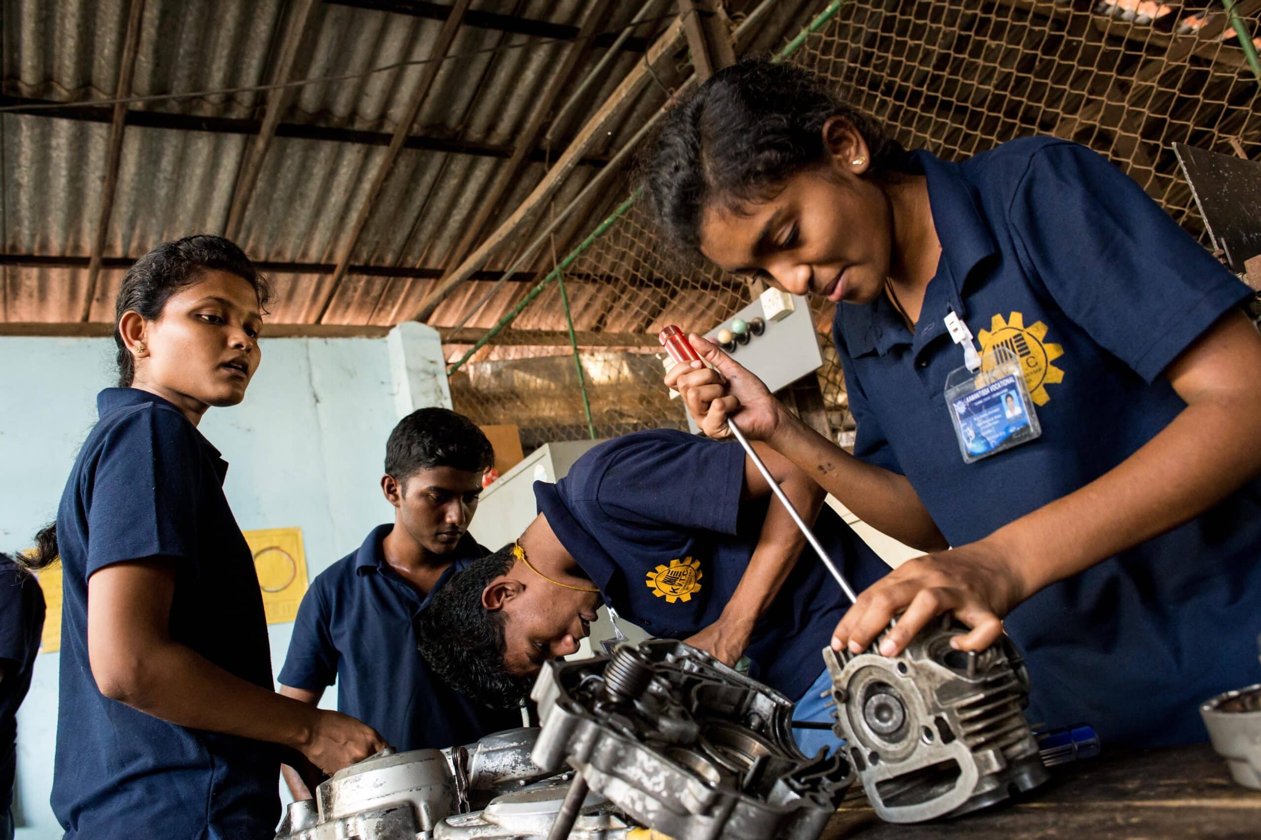 A group of young trainees in a automechanical program in Sri Lanka work on a car engine together.